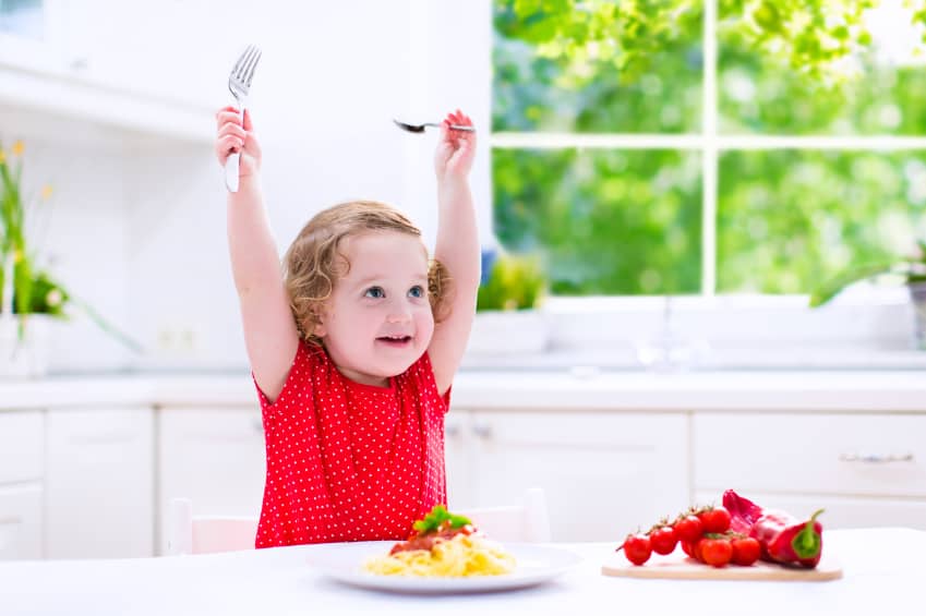 Kids eat pasta. Healthy lunch for children. Toddler kid eating spaghetti Bolognese in a white kitchen at home. Preschooler child cooking noodles with tomato and pepper for dinner. Food for family.