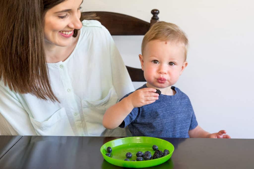 mom sitting side by side with boy toddler while watching son eating finger foods
