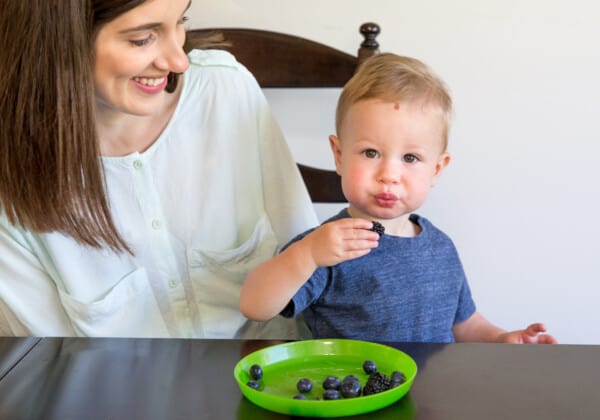mom sitting side by side with boy toddler while watching son eating finger foods