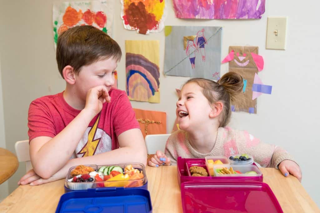 Zwei Kinder lachen miteinander, während sie ihr Mittagessen essen