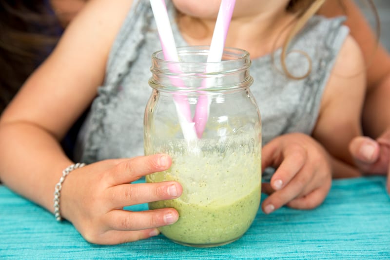 a child drinking a green smoothie from a straw