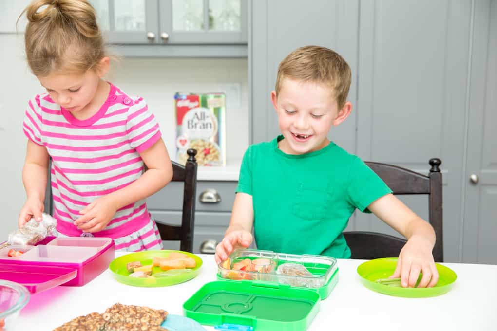 Zwei Kinder lächeln, während sie ihr Mittagessen für die Schule zubereiten