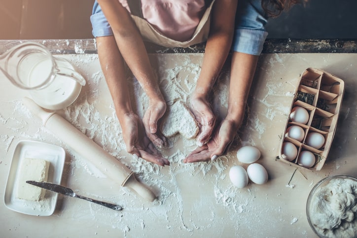 Parent and child baking together with flour and eggs.
