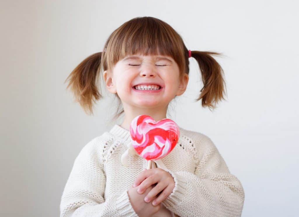 Excited child holding a lollipop and smiling.