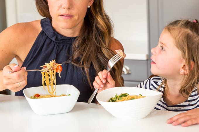 a mother and her daughter eat noodles from bowls at a table together