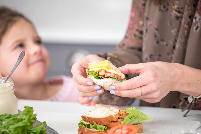 a mother holds a sandwich while her daughter looks up at her