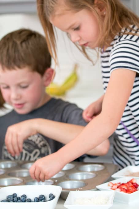 two young kids adding chopped fruits to muffin tins