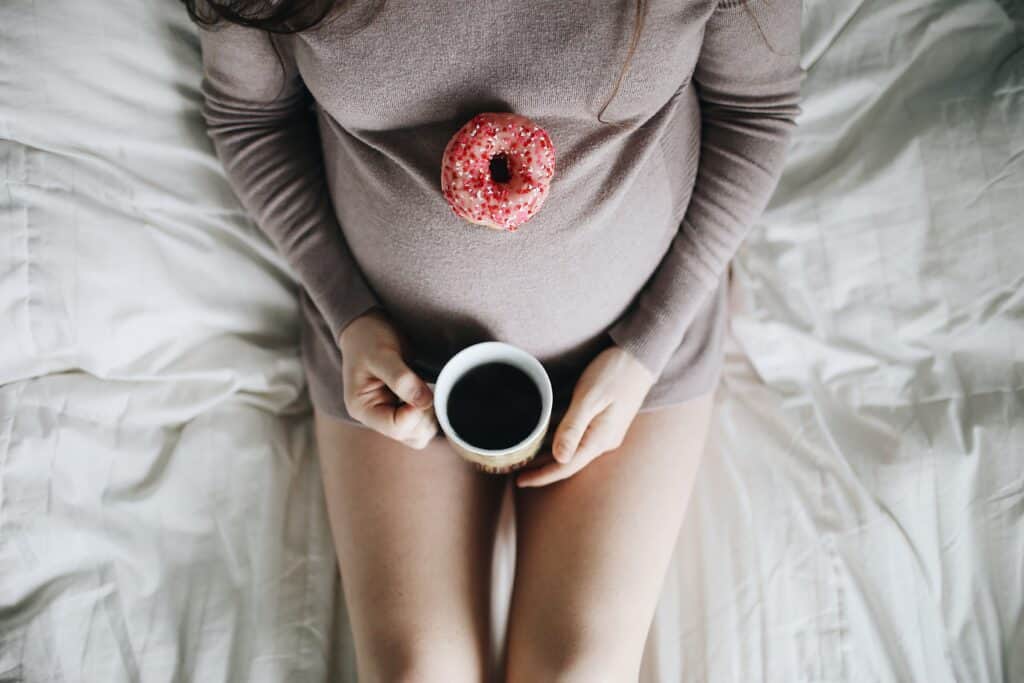 pregnant woman lying on a bed with a cup of coffee and a donut