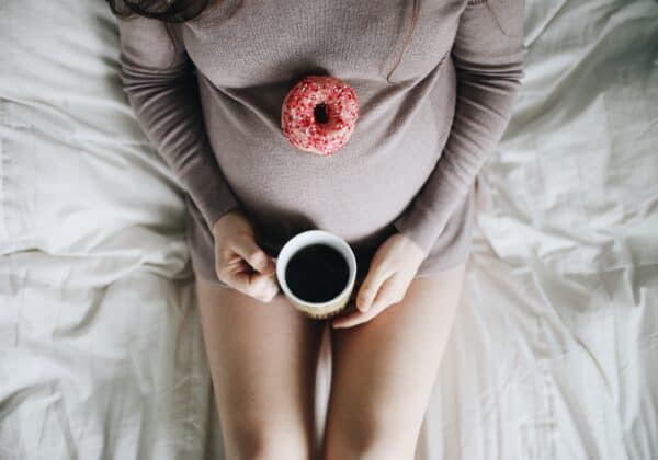 pregnant woman lying on a bed with a cup of coffee and a donut