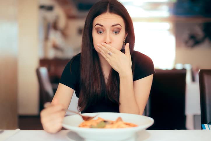 a pregnant woman eating at a table holding her mouth in disgust