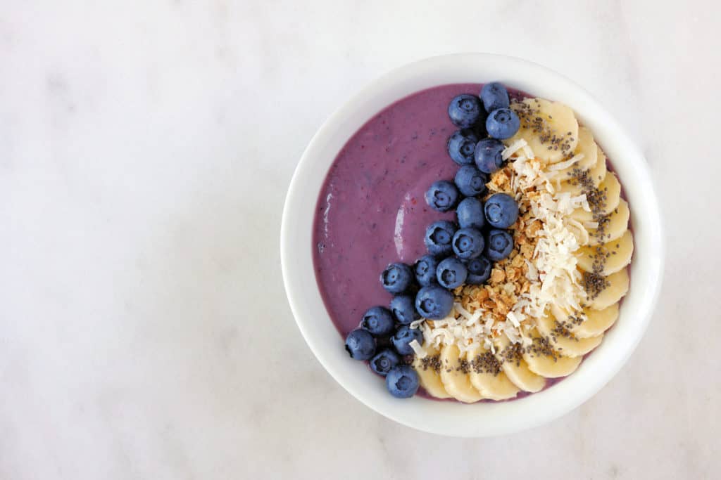 Healthy blueberry smoothie bowl with coconut, bananas, chia seeds and granola. Top view on a bright background.