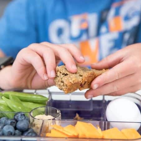 Close up of child holding granola bar above lunch box
