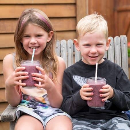 Two children sitting outside on a chair holding berry smoothies
