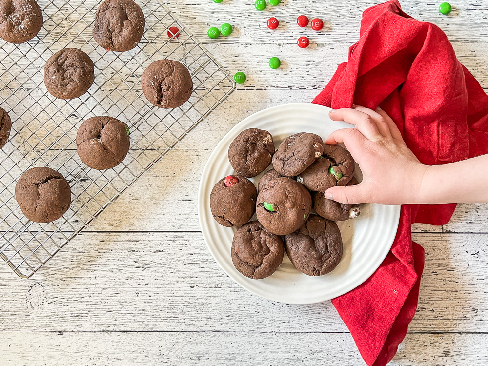 chocolate brownie cookies on a plate with child's hand grabbing one