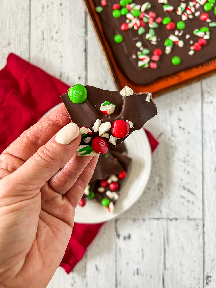 hand holding up a piece of chocolate bark with candy cane pieces