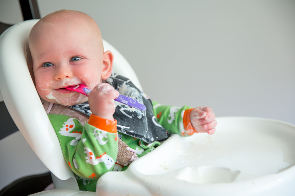 baby in a high chair eating yogurt with a spoon