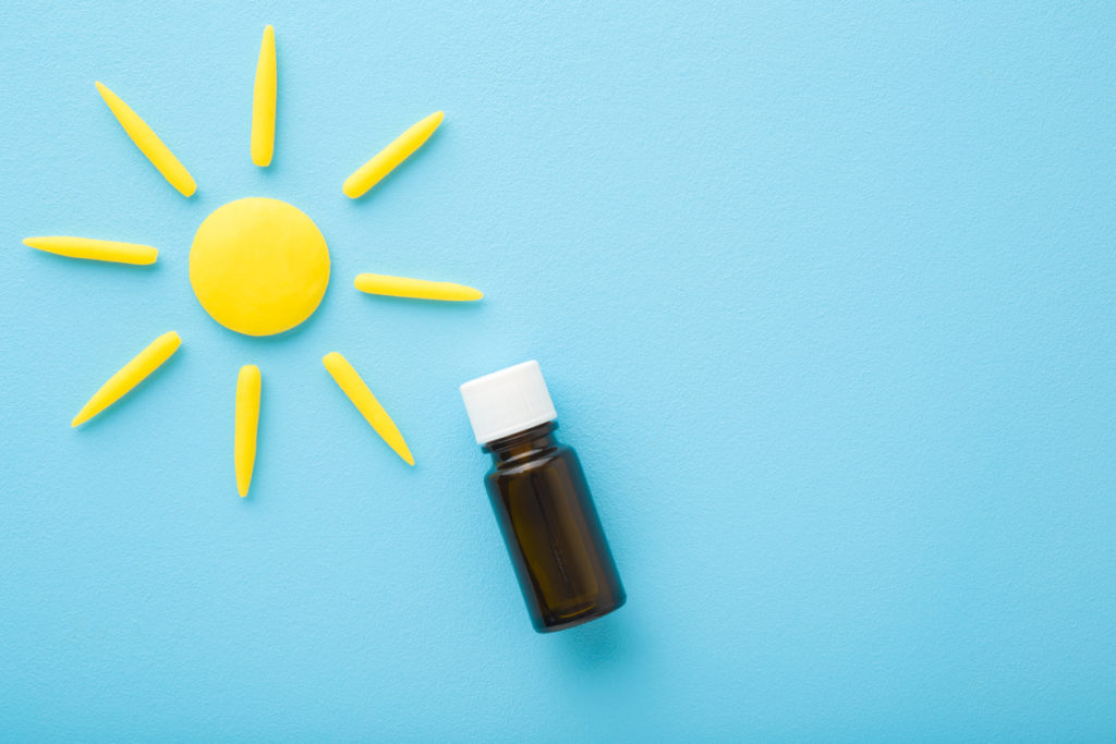 Brown glass bottle of d vitamin and yellow sun shape on light blue table background. Pastel color. Daily receiving vitamins. Closeup. Top down view.