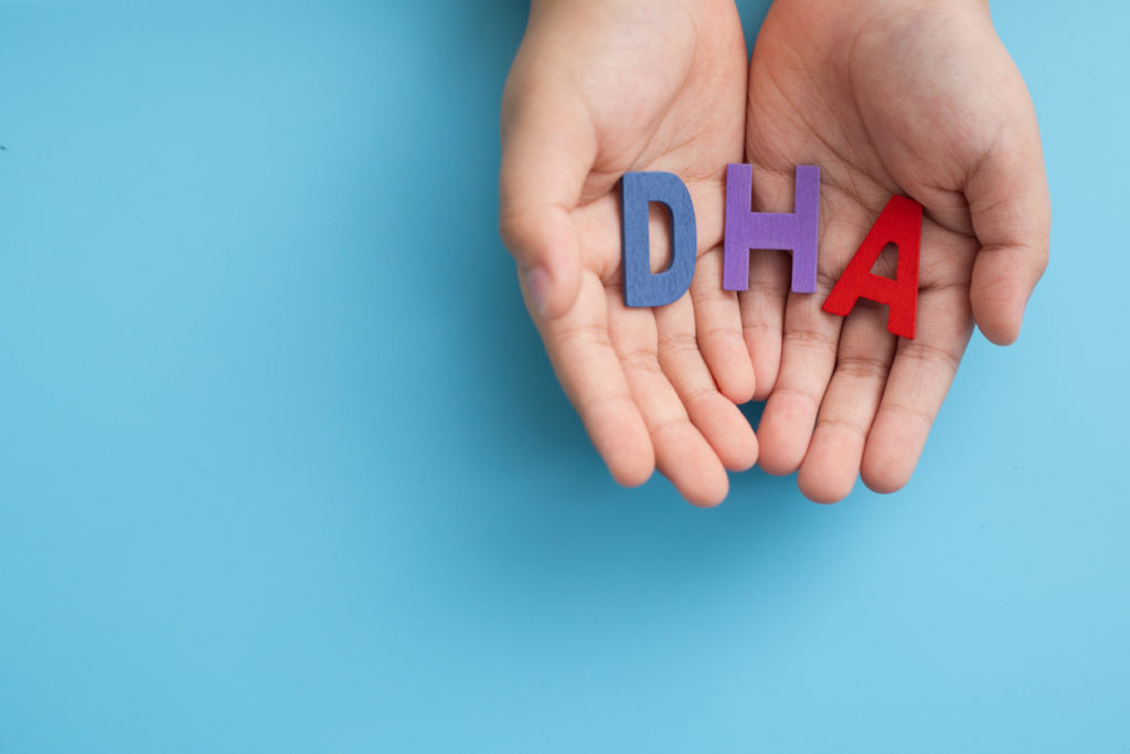 Hands showing multicolor wooden alphabet words "DHA" on blue background. Docosahexaenoic acid is an omega-3 fatty acid that is a primary structural component of the human brain, cerebral cortex, skin, and retina.