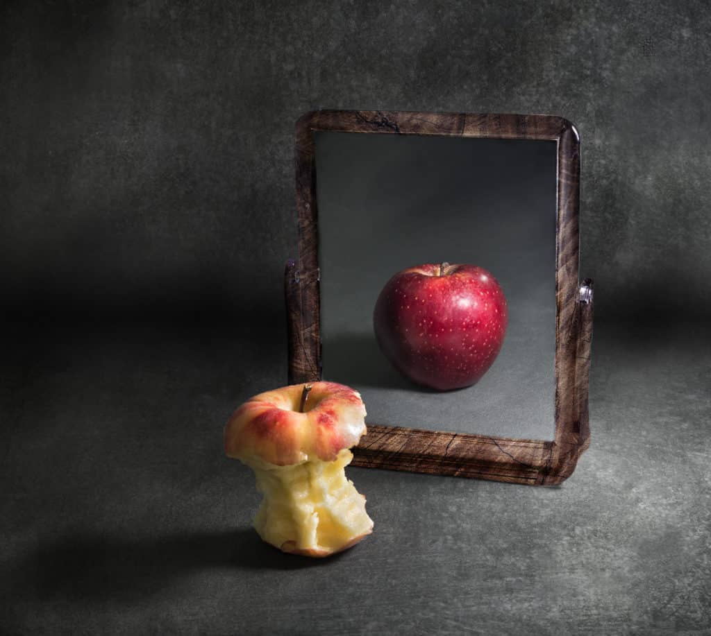 apple with poor body image looking at its reflection in a mirror With grey background