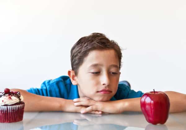 A young boy deciding between a cupcake and an apple.