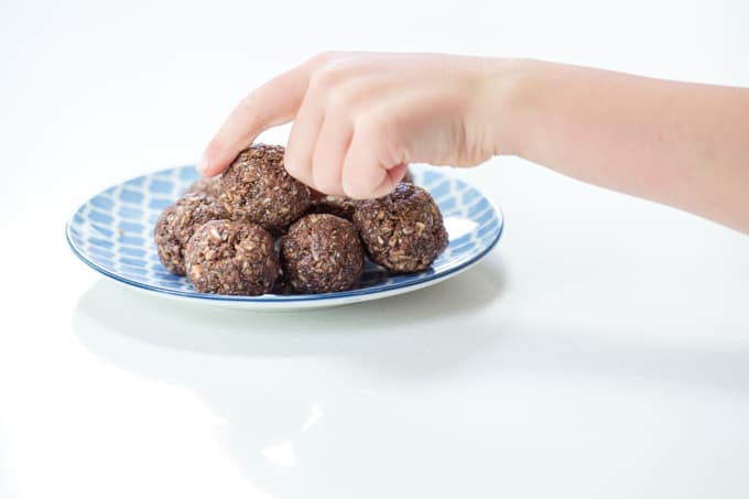 Double chocolate chia protein balls with a child's handing reaching for one off of a blue plate.