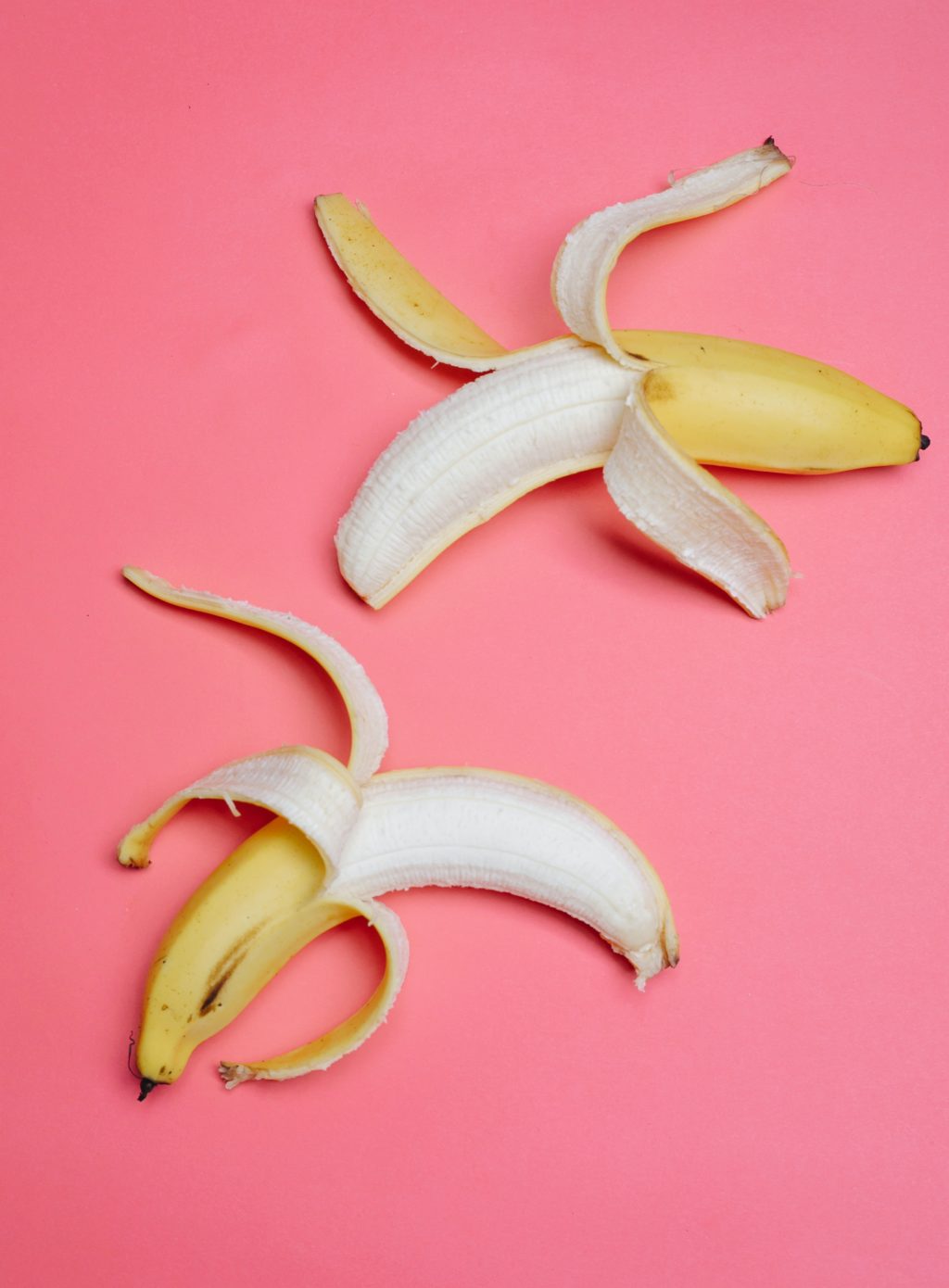 Two peeled bananas on a pink surface