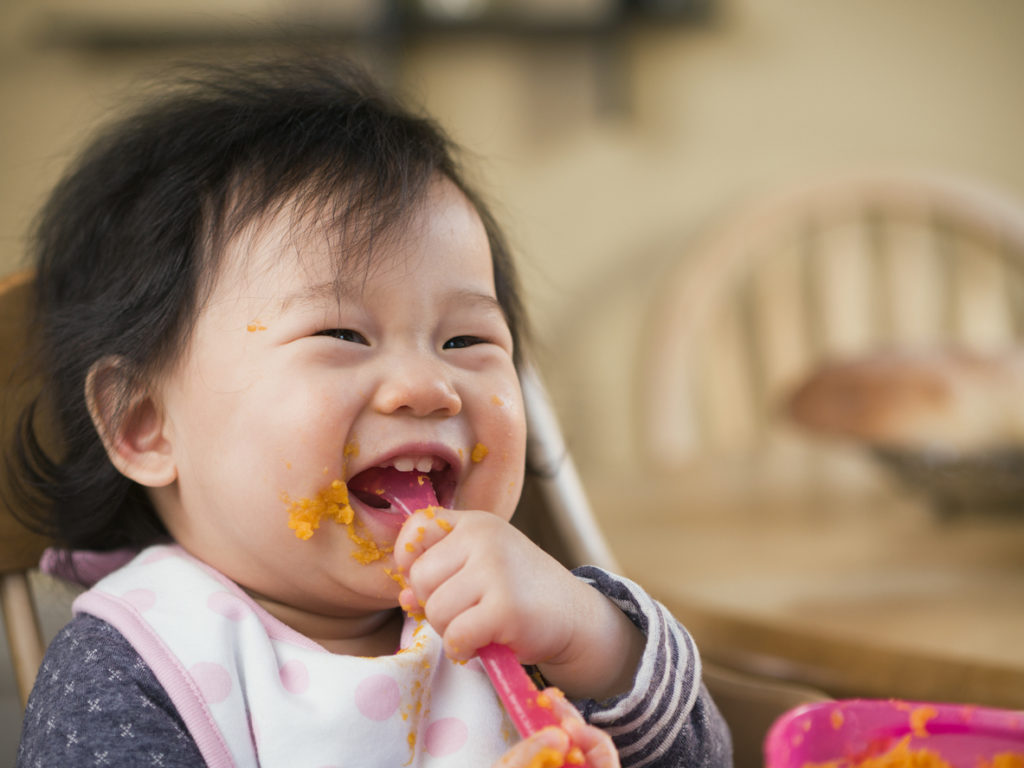 Babymädchen füttern sich mit einem Löffel Süßkartoffelpüree