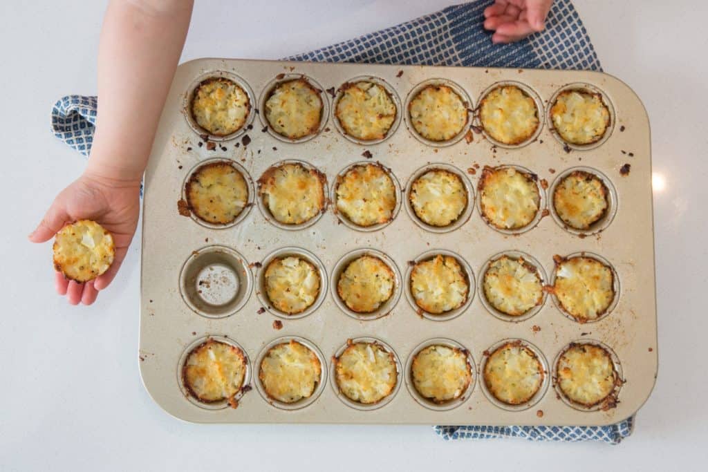 caulitots in a mini muffin pan with a hand holding one out