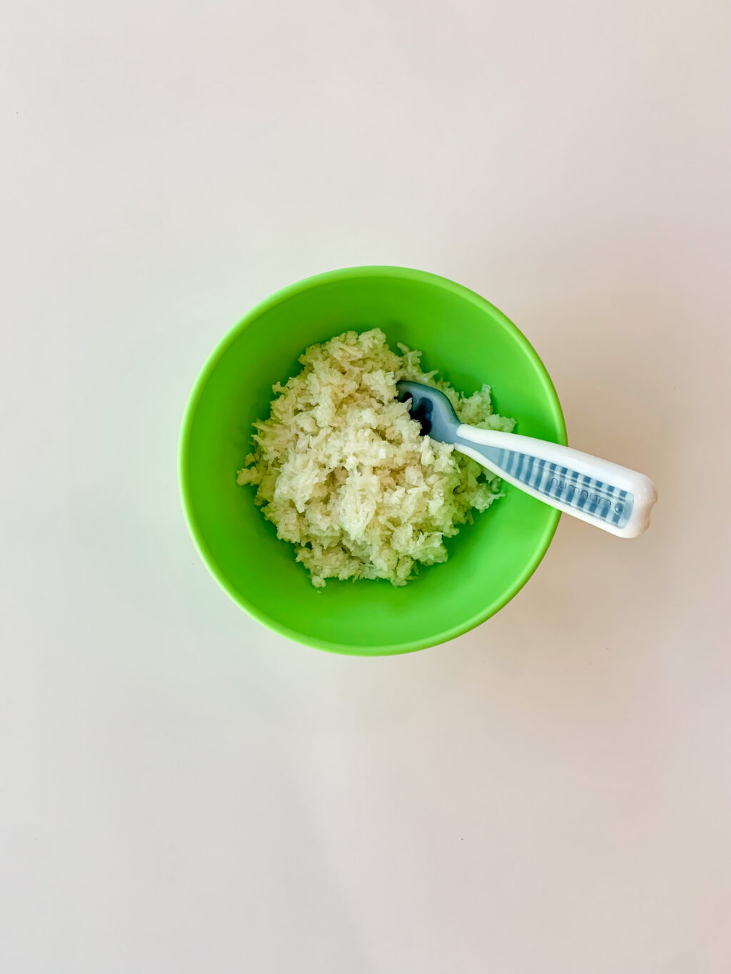 mashed cooked cauliflower in a green bowl with baby spoon