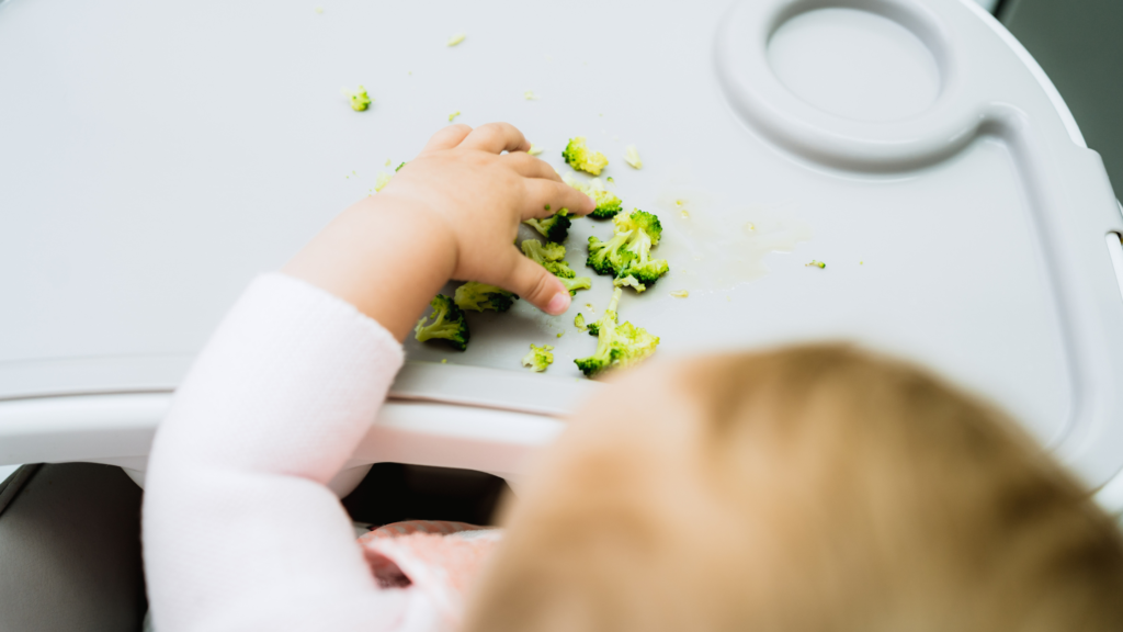 a baby feeding herself soft pieces of broccoli