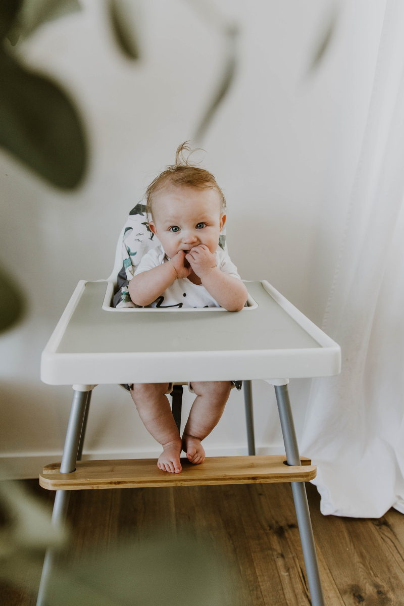 a cute baby with hands in his mouth sitting in a highchair