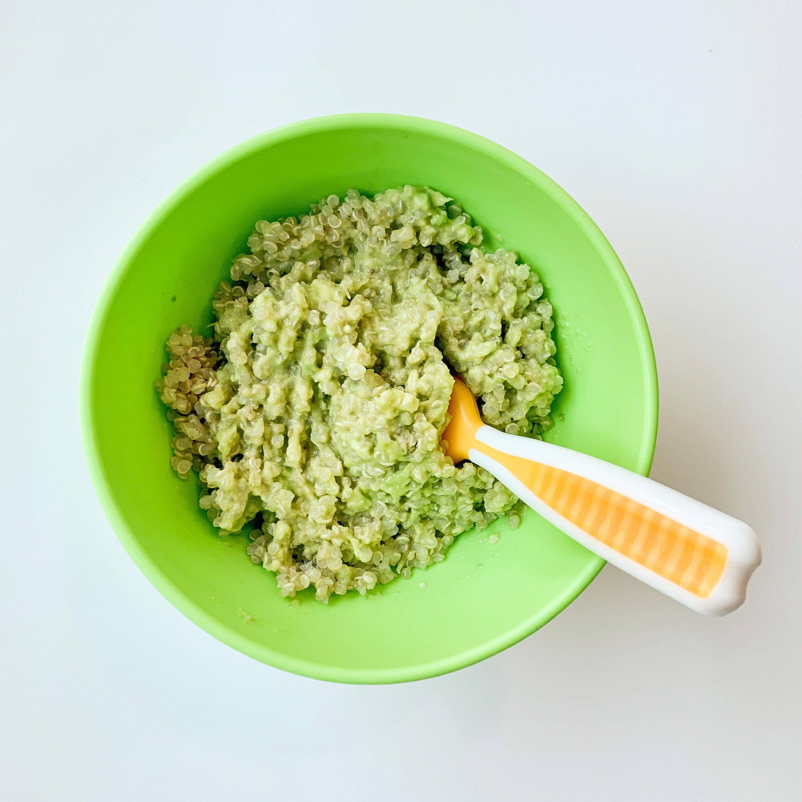 top view of cooked quinoa with mashed avocado and a baby spoon