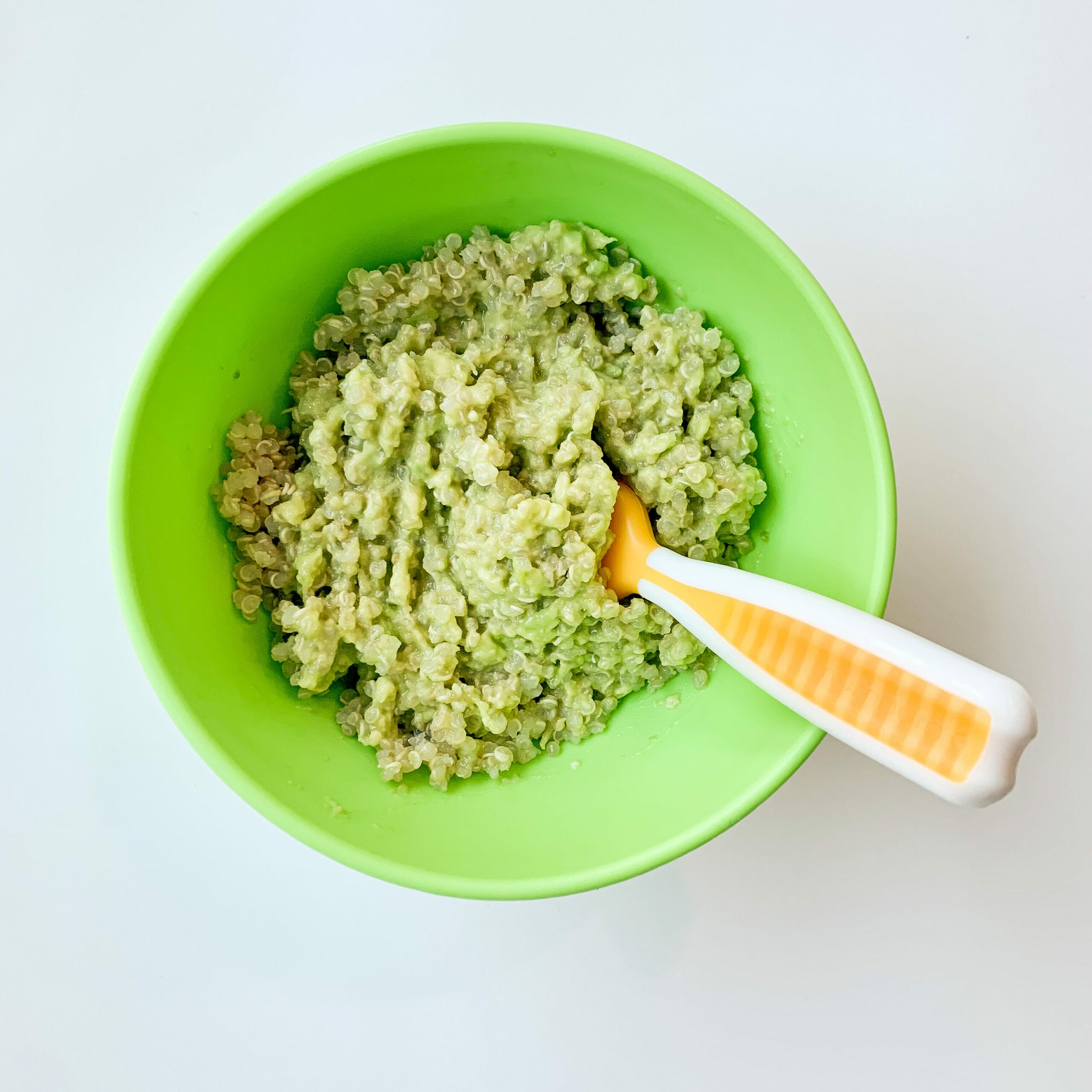 top view of cooked quinoa with mashed avocado and a baby spoon