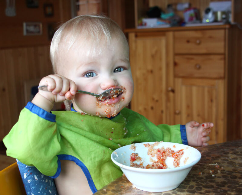 baby eats with a spoon quinoa with vegetables from a bowl