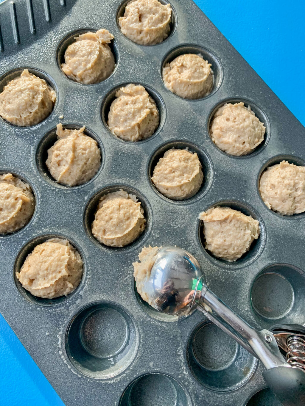 muffin batter being scooped into a mini muffin tin tray