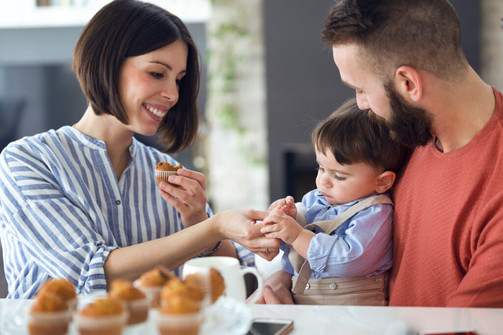 Shot of beautiful young parents with they baby eating muffins at home