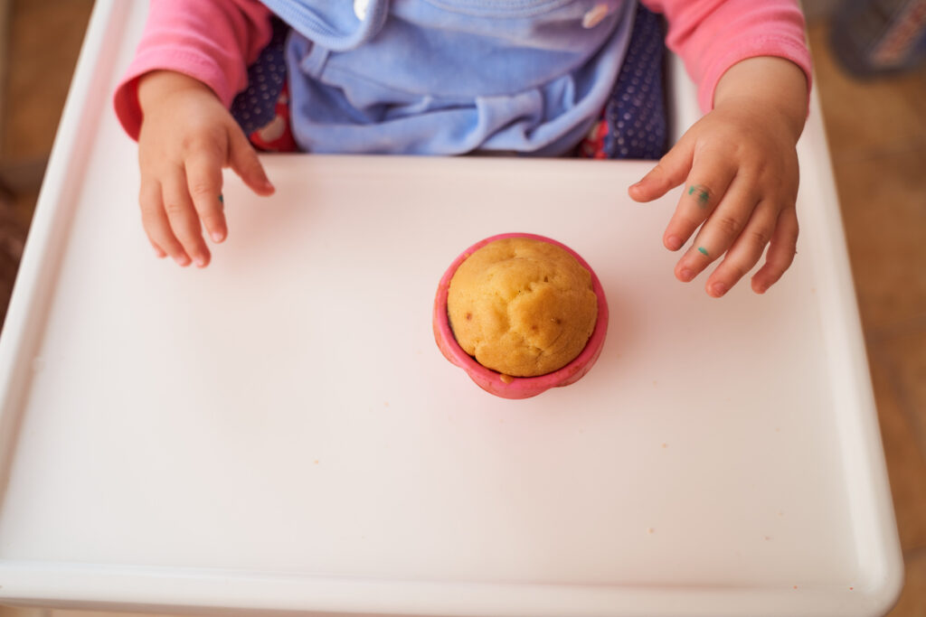 A baby holds a homemade muffin sitting at a high chair