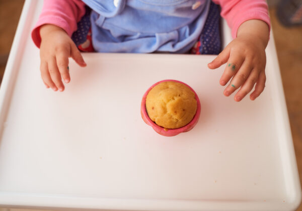 A baby holds a homemade muffin sitting at a high chair