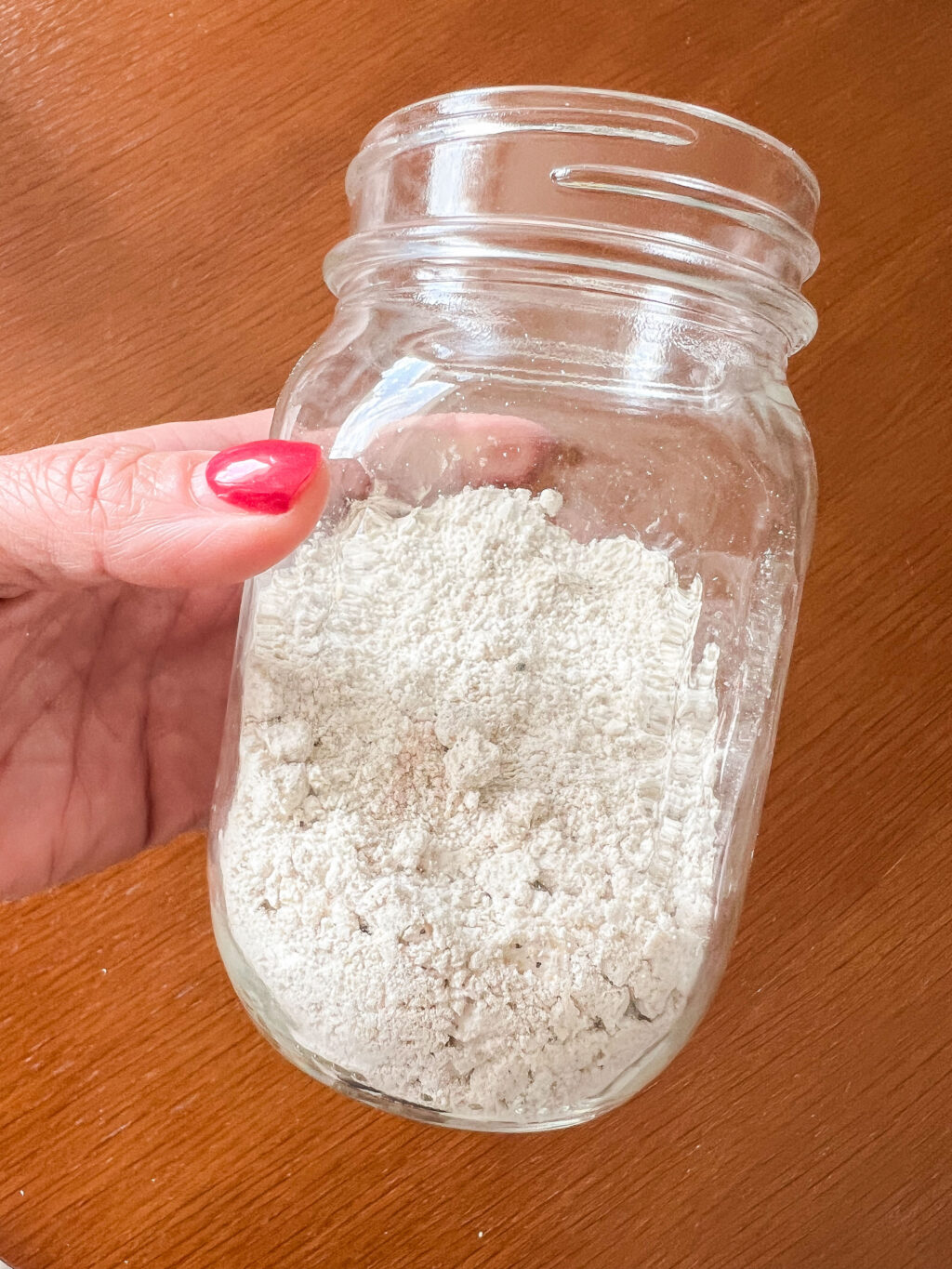 close up of a hand holding a mason jar full of ground oat flour