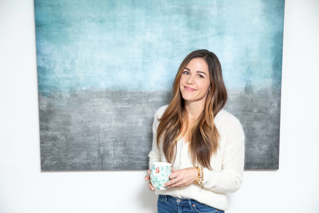 close up of Sarah holding a coffee cup smiling at the camera