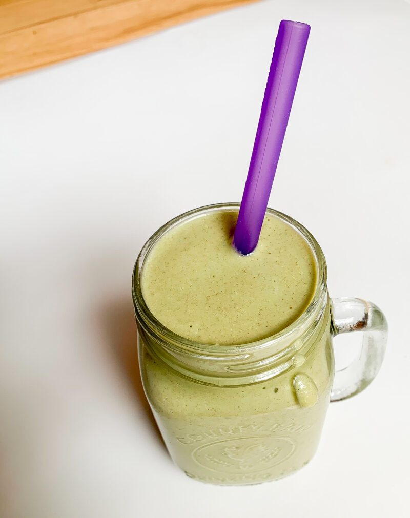 close up of a green banana date smoothie in a glass jar with a purple straw