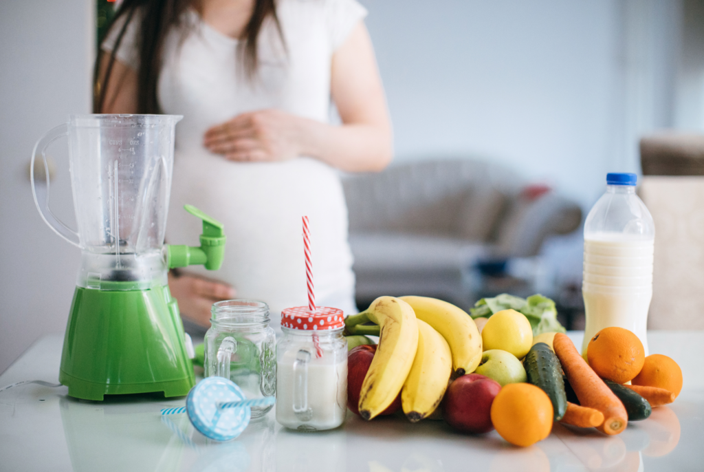 close up of a pregnant woman making a smoothie with a bunch of fruits and vegetables on a counter