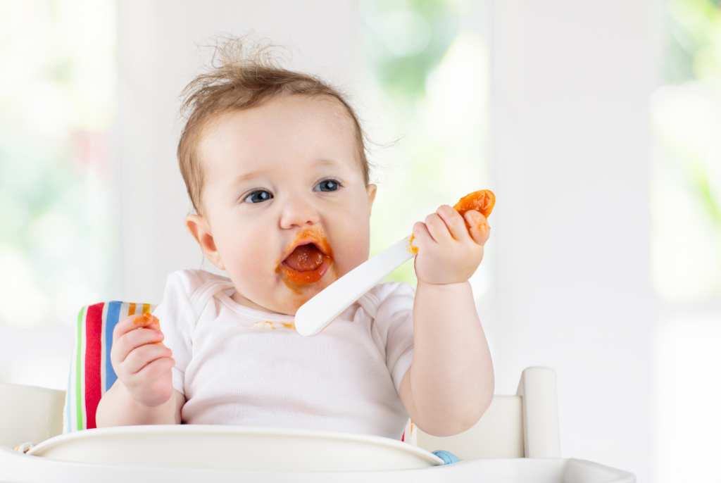 close up of a happy baby learning to eat pureed carrots in a high chair