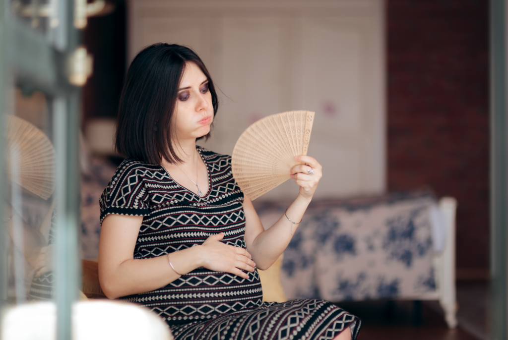a nauseous pregnant woman holding a fan