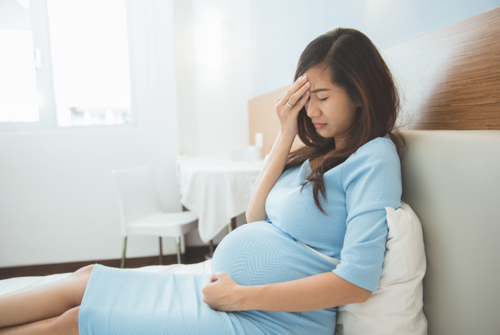side view of a stressed pregnant woman sitting on a bed