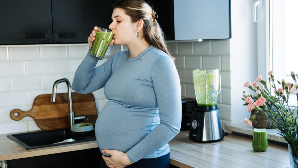 a pregnant woman drinking a green smoothie
