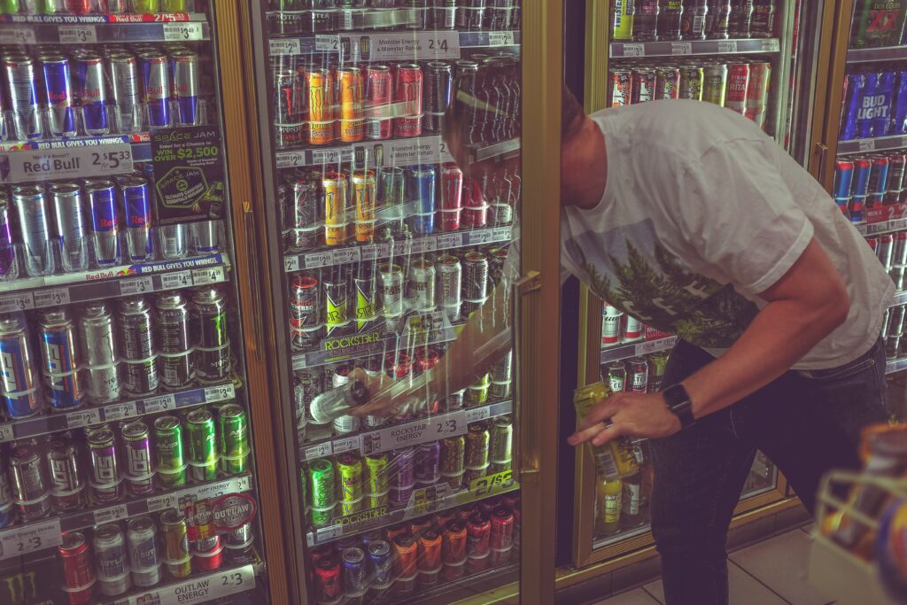 a teen reaching for an energy drink from a convenience store fridge