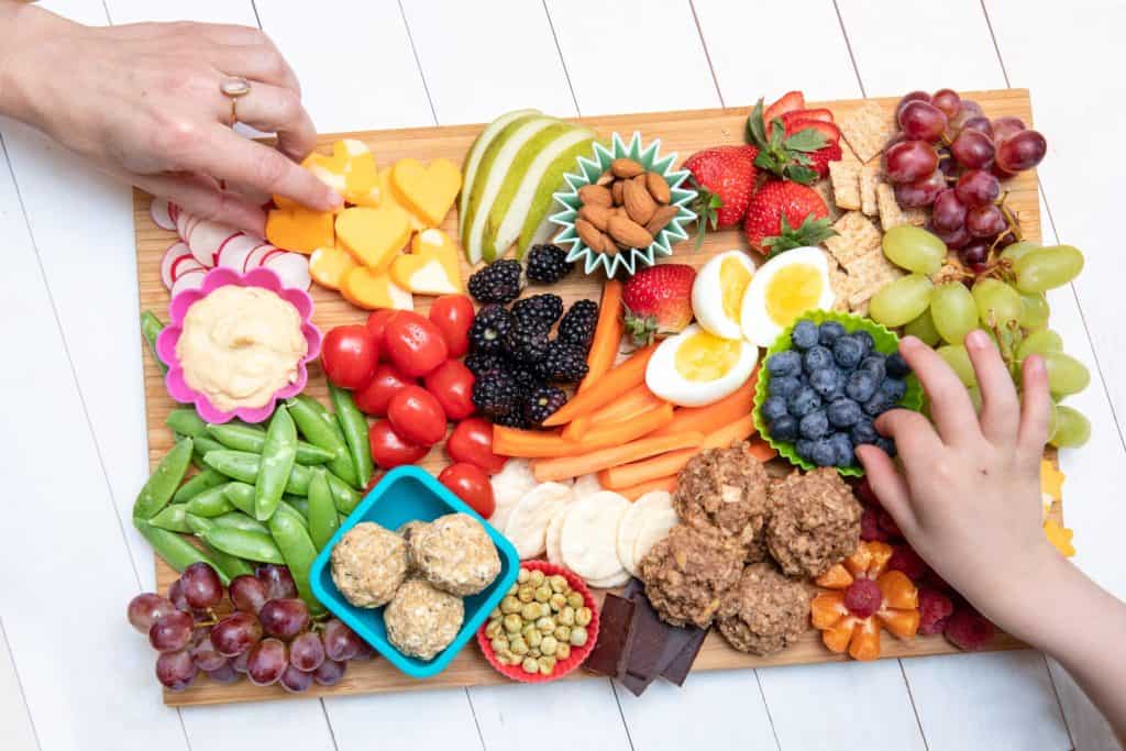 top down view of a snack board filled with tasty lunch options including fruits, veggie sticks, muffins, eggs and more