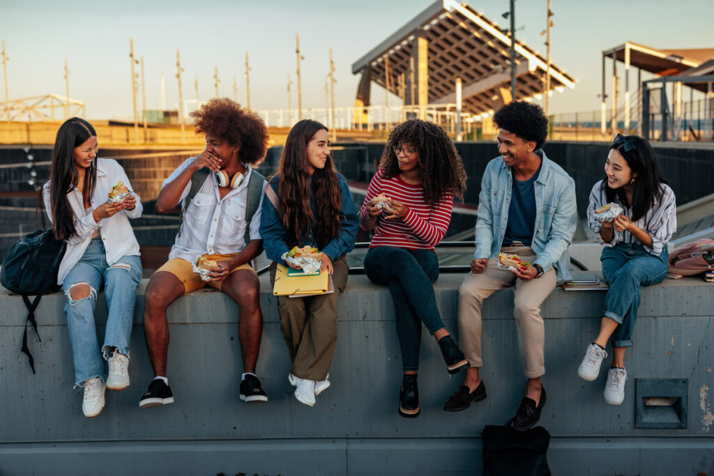 side view of a bunch of teens sitting on a concrete ledge eating food together