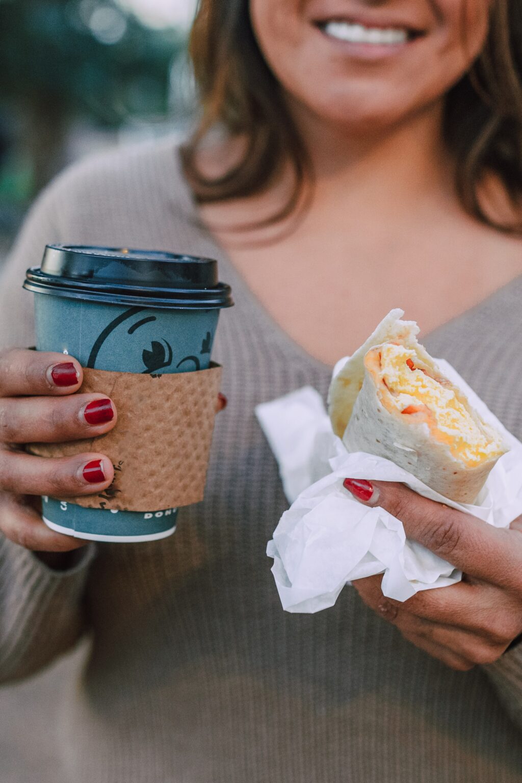 a girl holding a whole wheat wrap with a cup of coffee